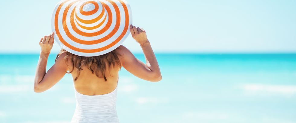 young woman in hat standing on beach rear view