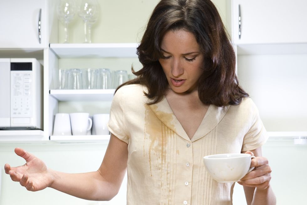 Young woman in kitchen, coffee spilit on shirt
