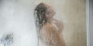 Young woman in shower behind steamed glass door