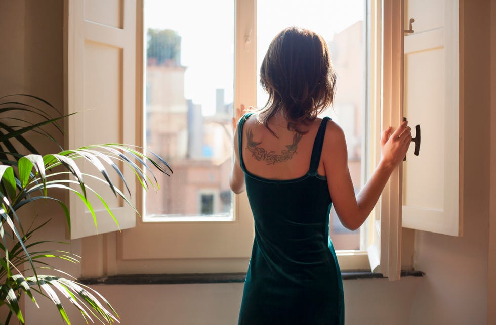 una mujer joven se dispone a abrir la ventana en su casa