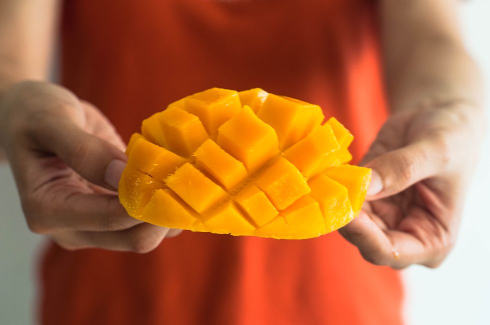 a young woman is holding a freshly sliced ripe mango