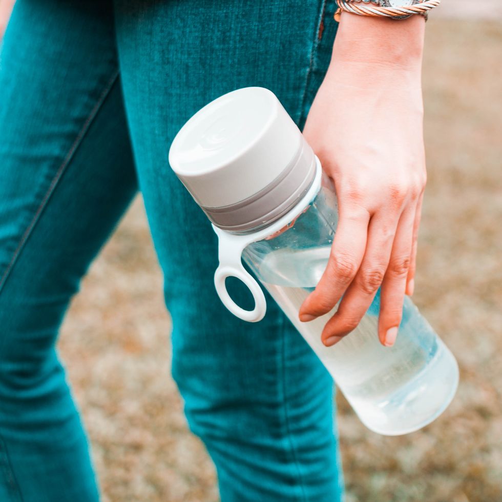 a young woman is holding a reusable water bottle container outdoors