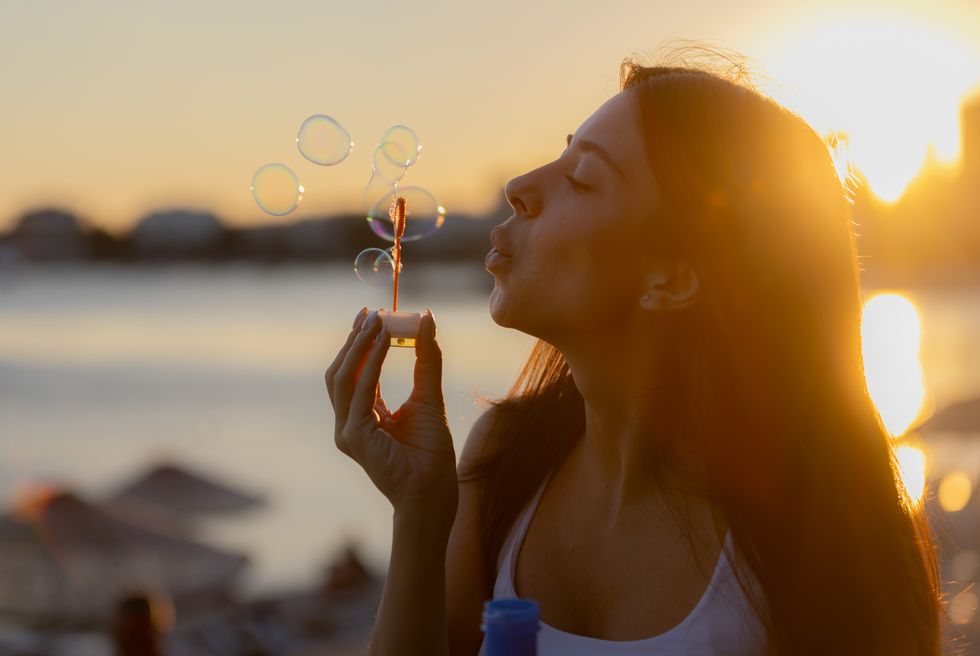 young woman is playing with bubble wand at sunset