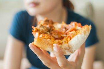 a young woman is spending her time eating a slice of pizza white sitting on a couch