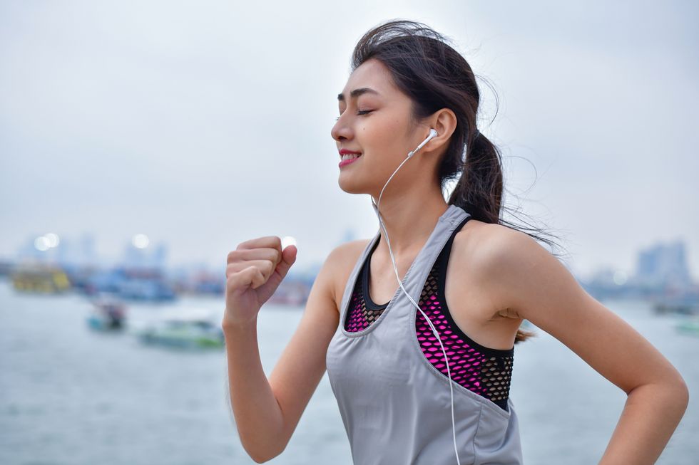 young woman jogging on footpath while listening music in city