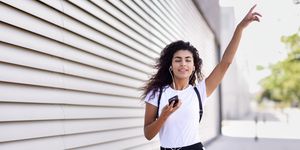 Young Woman Listening Music While Walking On Footpath By Wall