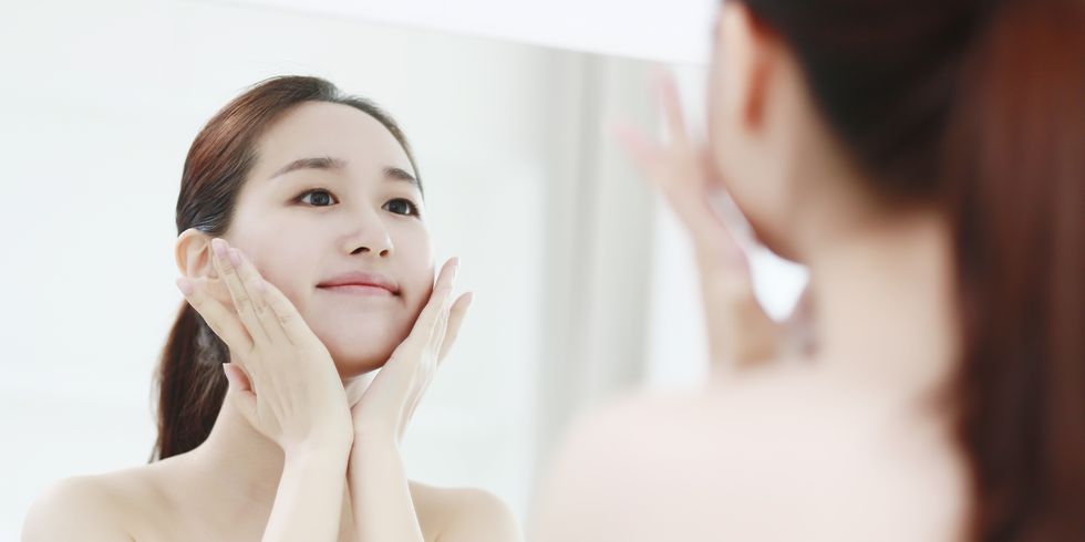 young woman looking in mirror, touching face