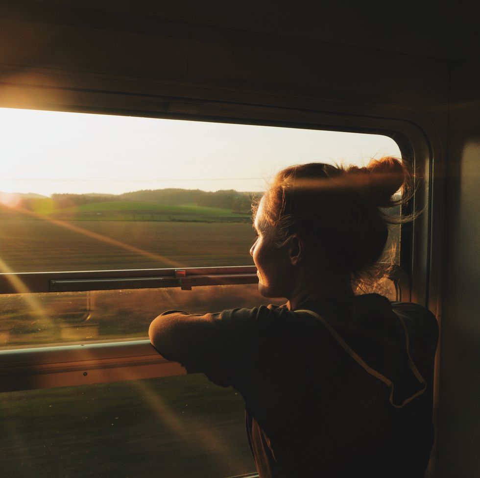 young woman looking through window while traveling in train during sunset