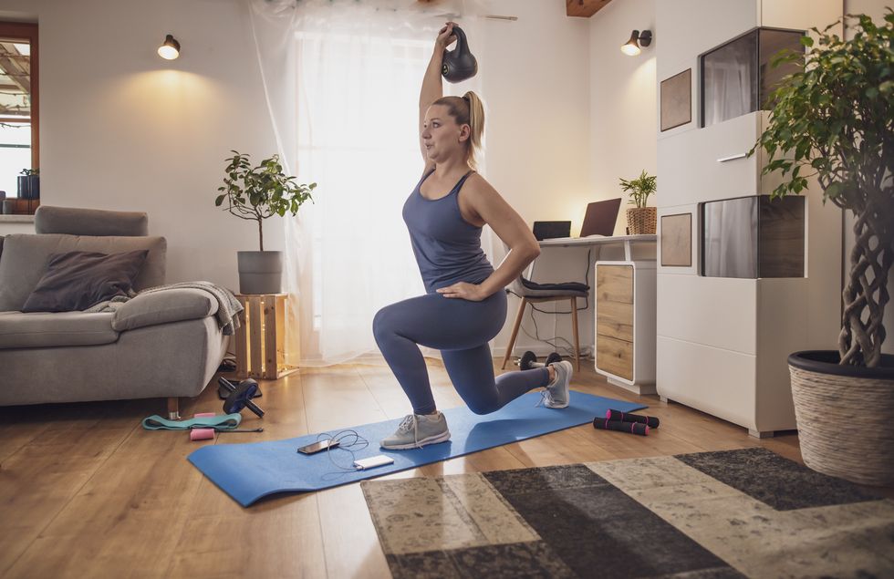 young woman lunging with kettlebell on yoga mat in living room