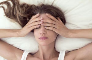 young woman lying in bed and covering eyes