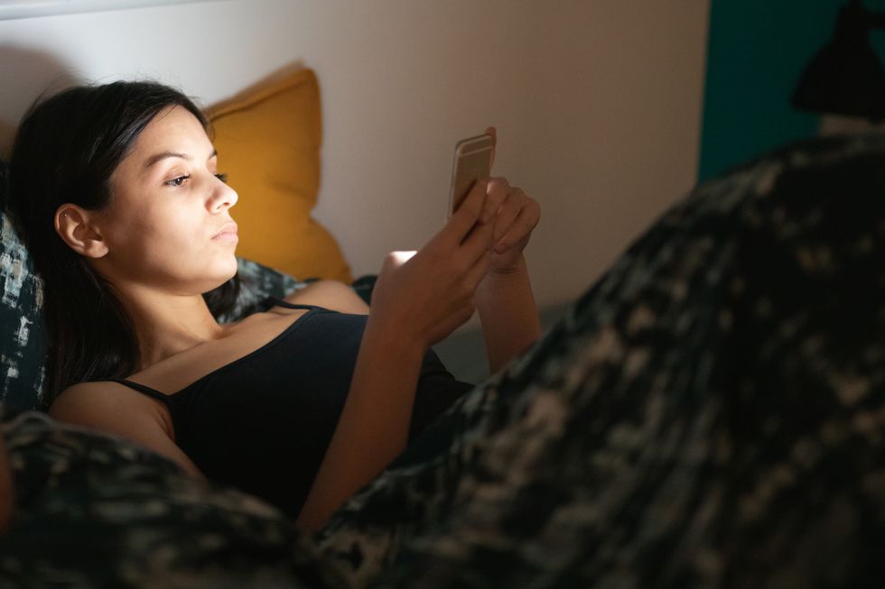 young woman lying in bed at night and using online dating app