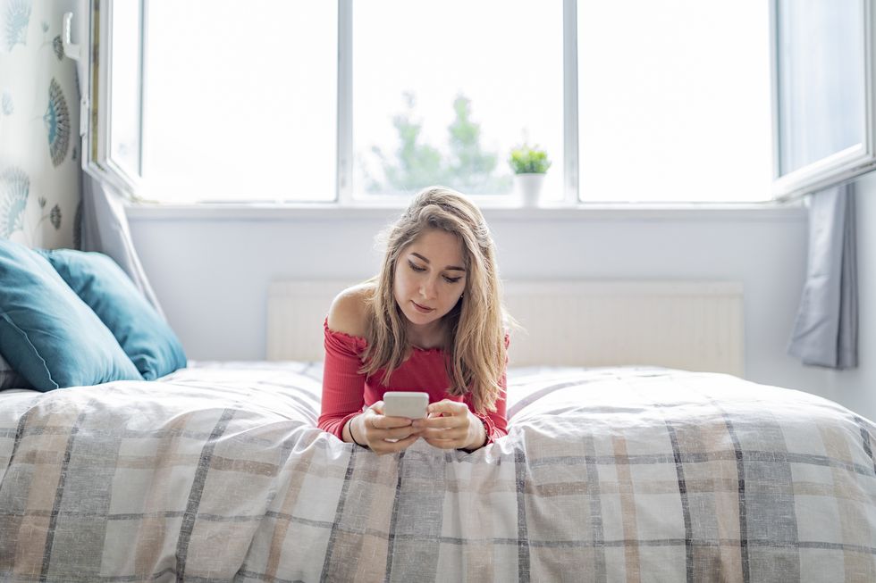 young woman lying on bed at home using cell phone