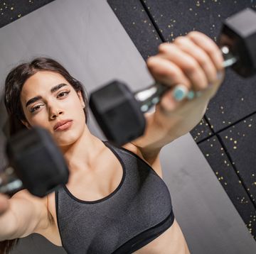 young woman lying on the exercise mat and doing exercises with dumbbell