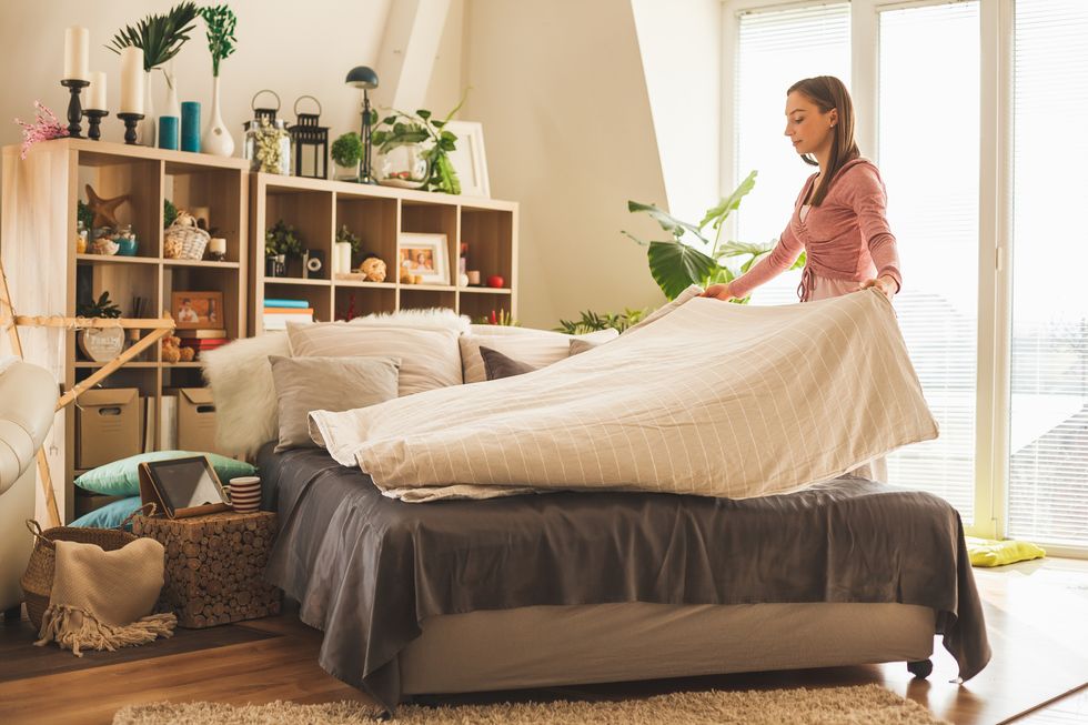 Young woman making bed at home