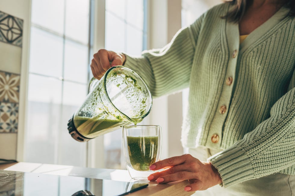 young woman making detox smoothie at home woman pouring smoothie to glass healthy food concept