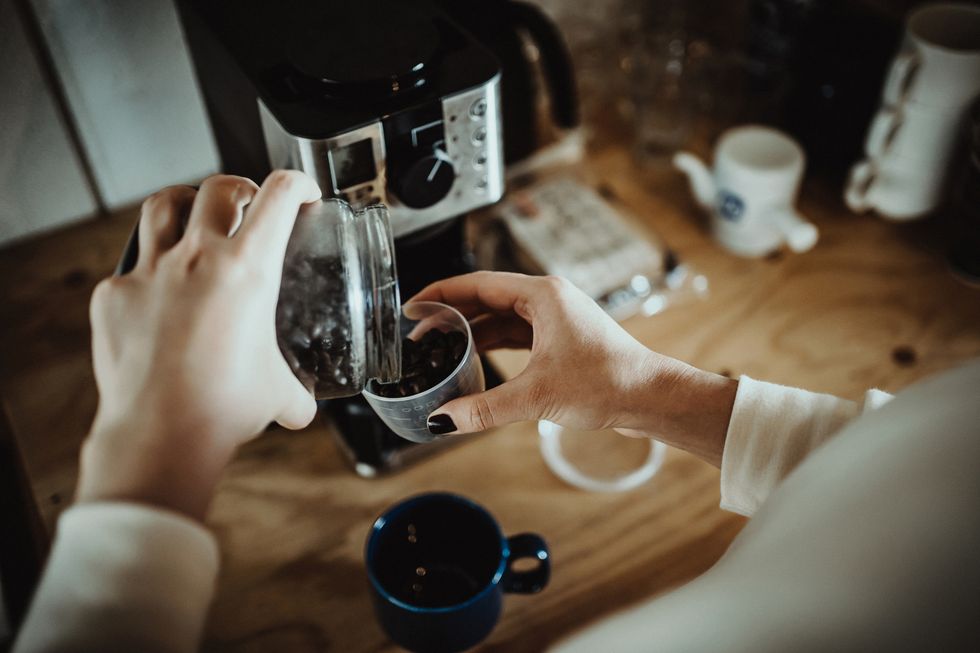 young woman measuring and pouring roasted coffee beans into coffee machine and preparing coffee at home in the early morning