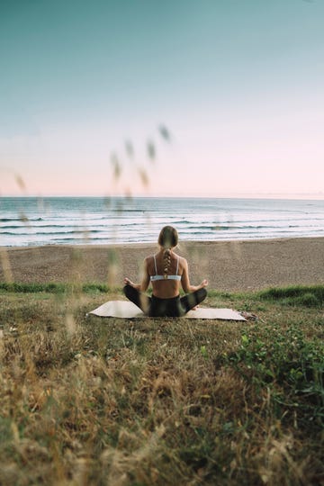 young woman meditating at beach against clear sky during sunset