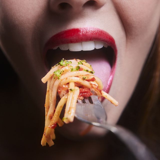 young woman mouth eating spaghetti pasta bolognese on a silver fork