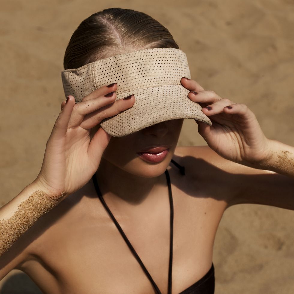 young woman on beach, wearing sun visor, elevated view