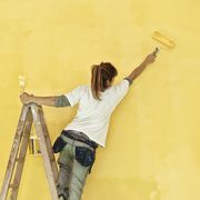 Young woman painting wall with yellow paint