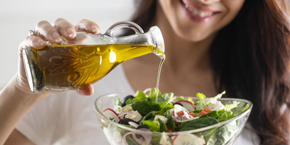 young woman pouring olive oil in to the salad healthy lifestyle eating concept