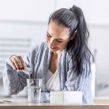 a young woman pours magnesium nutritional supplement into a glass of water