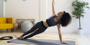 young woman practicing side plank pose in living room