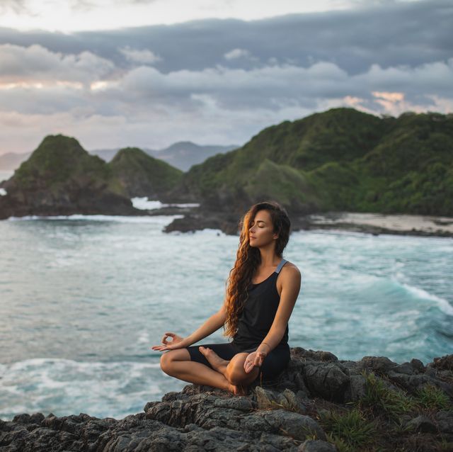 young woman practicing yoga in lotus pose at sunset with beautiful ocean and mountain view sensitivity to nature self analysis and soul searching spiritual and emotional concept