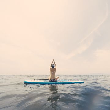 young woman practicing yoga on a paddleboard in the ocean