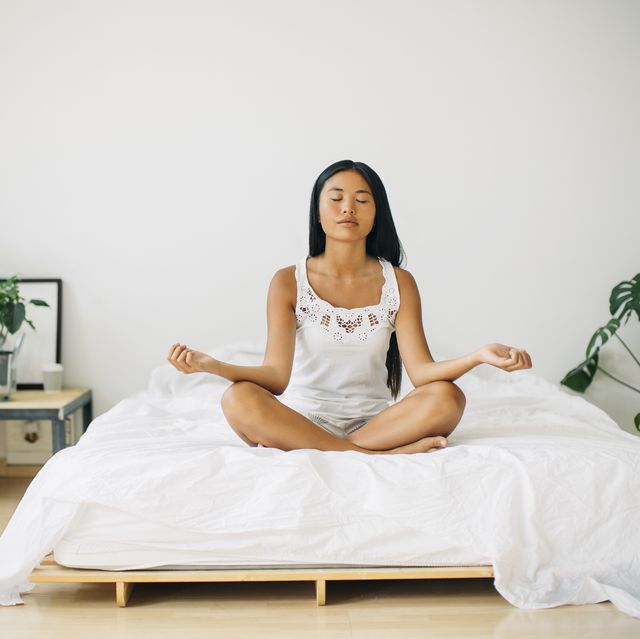 young woman practicing yoga on bed