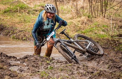 young woman pushing her mountain bike after falling in a muddy puddle
