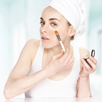 Una mujer joven se aplica corrector de ojeras una chica joven se pone, con pincel, un producto para corregir las ojeras