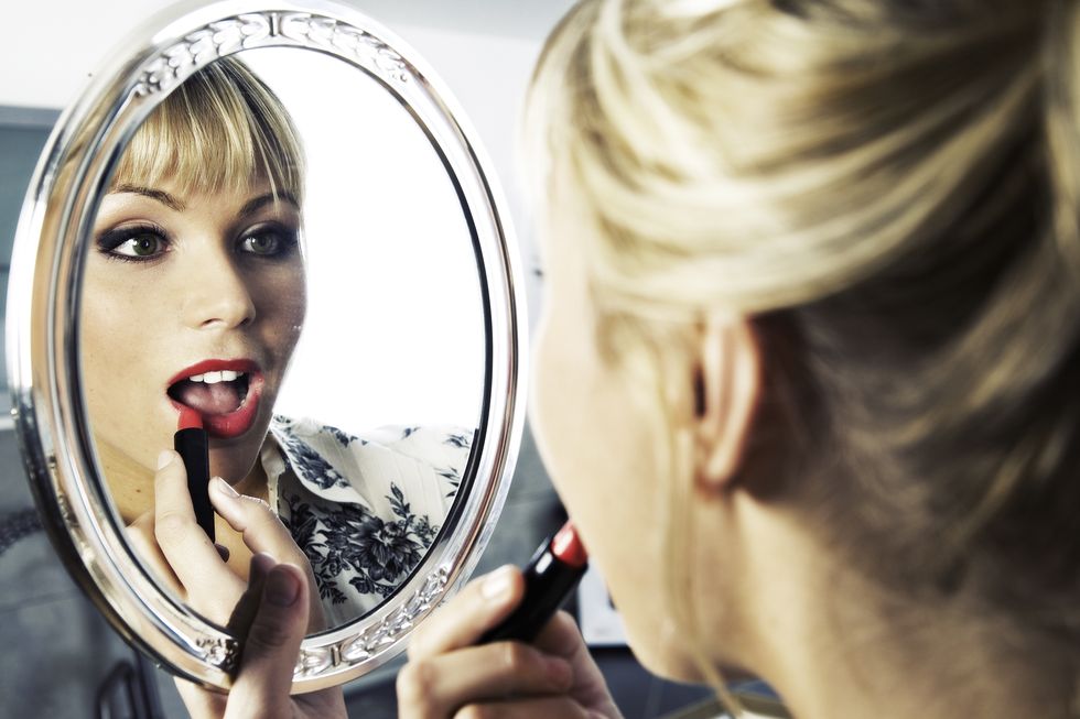 Young Woman Putting on Lipstick Looking in the Mirror