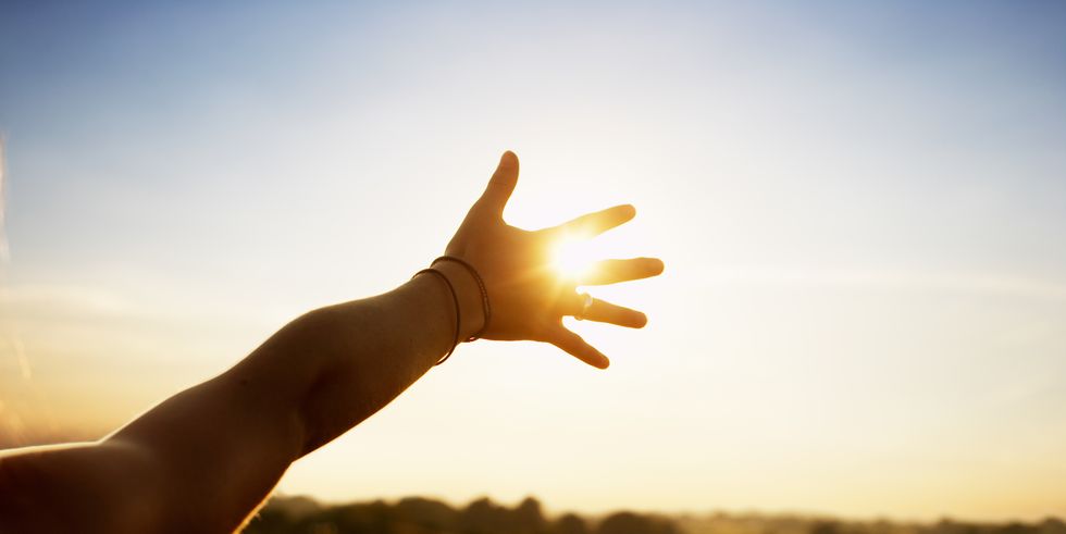 young woman reaching hand towards sun