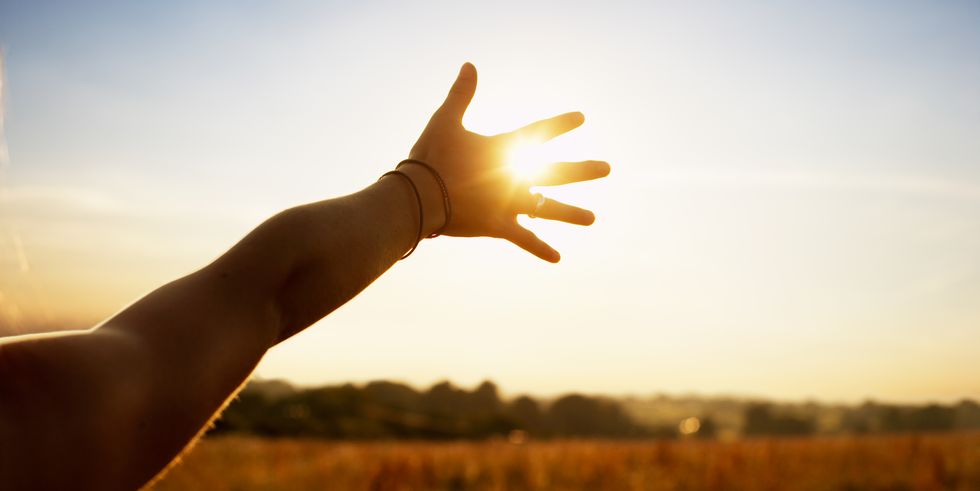 young woman reaching hand towards sun