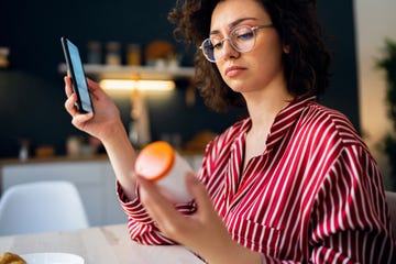 young woman reading a medicine prescription on her smart phone while holding a pill bottle