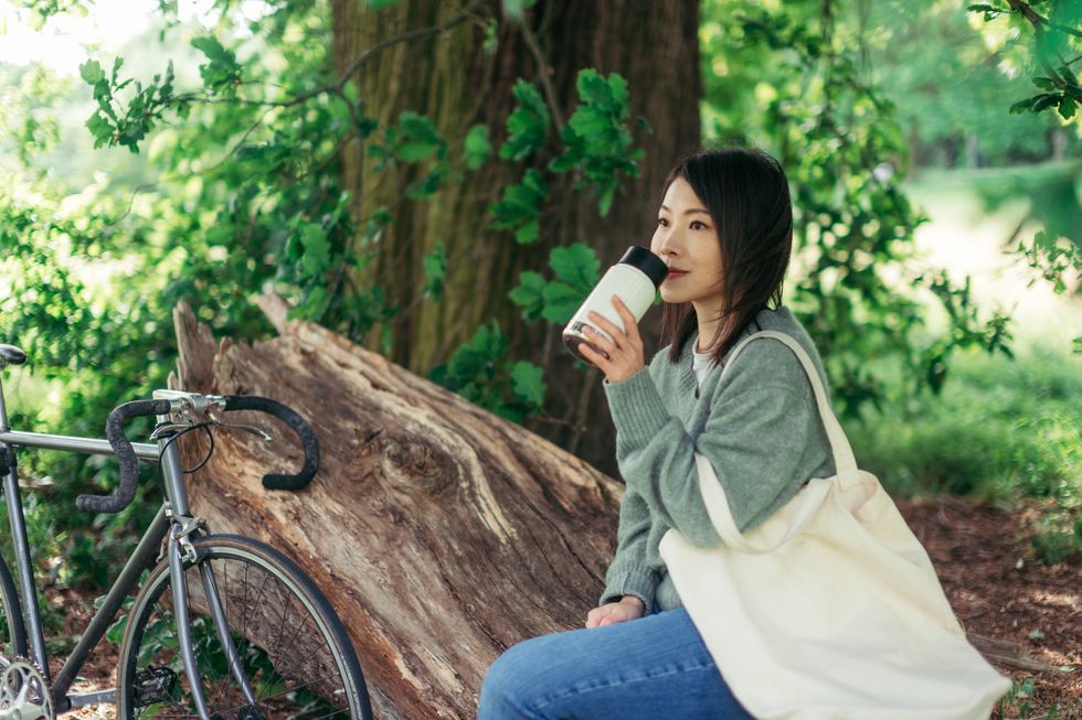 young woman relaxing in nature, drinking with a reusable coffee cup