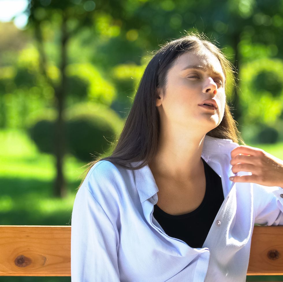 young woman resting on bench in park suffering from heat and stuffiness, pms