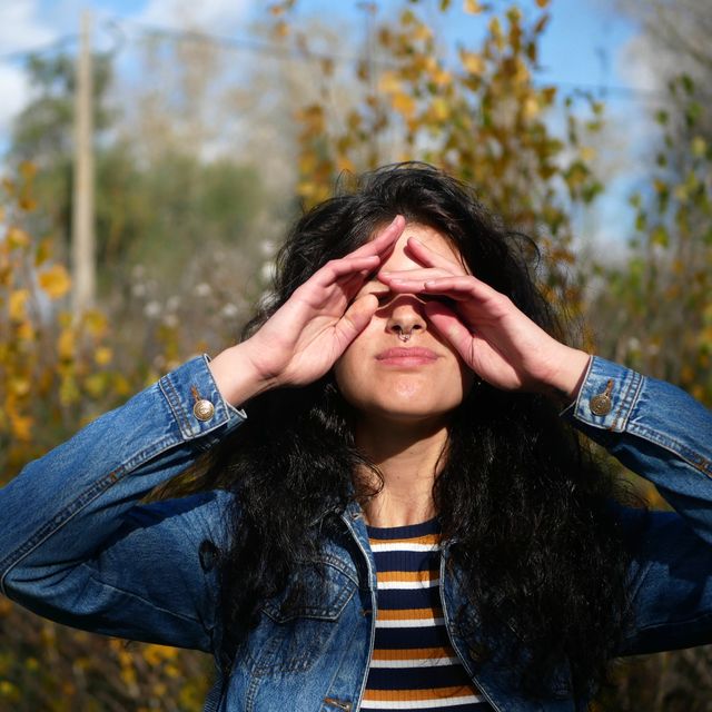 young woman rubbing eyes while standing against trees in forest
