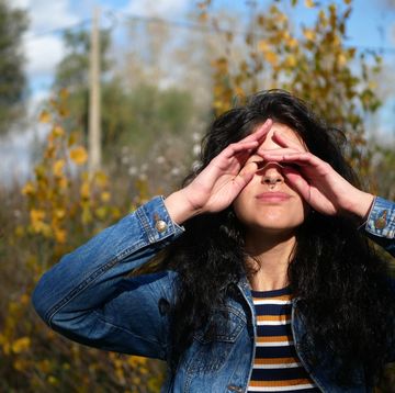 young woman rubbing eyes while standing against trees in forest