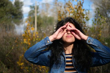 young woman rubbing eyes while standing against trees in forest