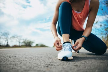 a young woman runner is outside in the morning, preparing for a jog she is seen bending down, tying her shoelaces, ensuring her running shoes are securely fastened before she begins her run