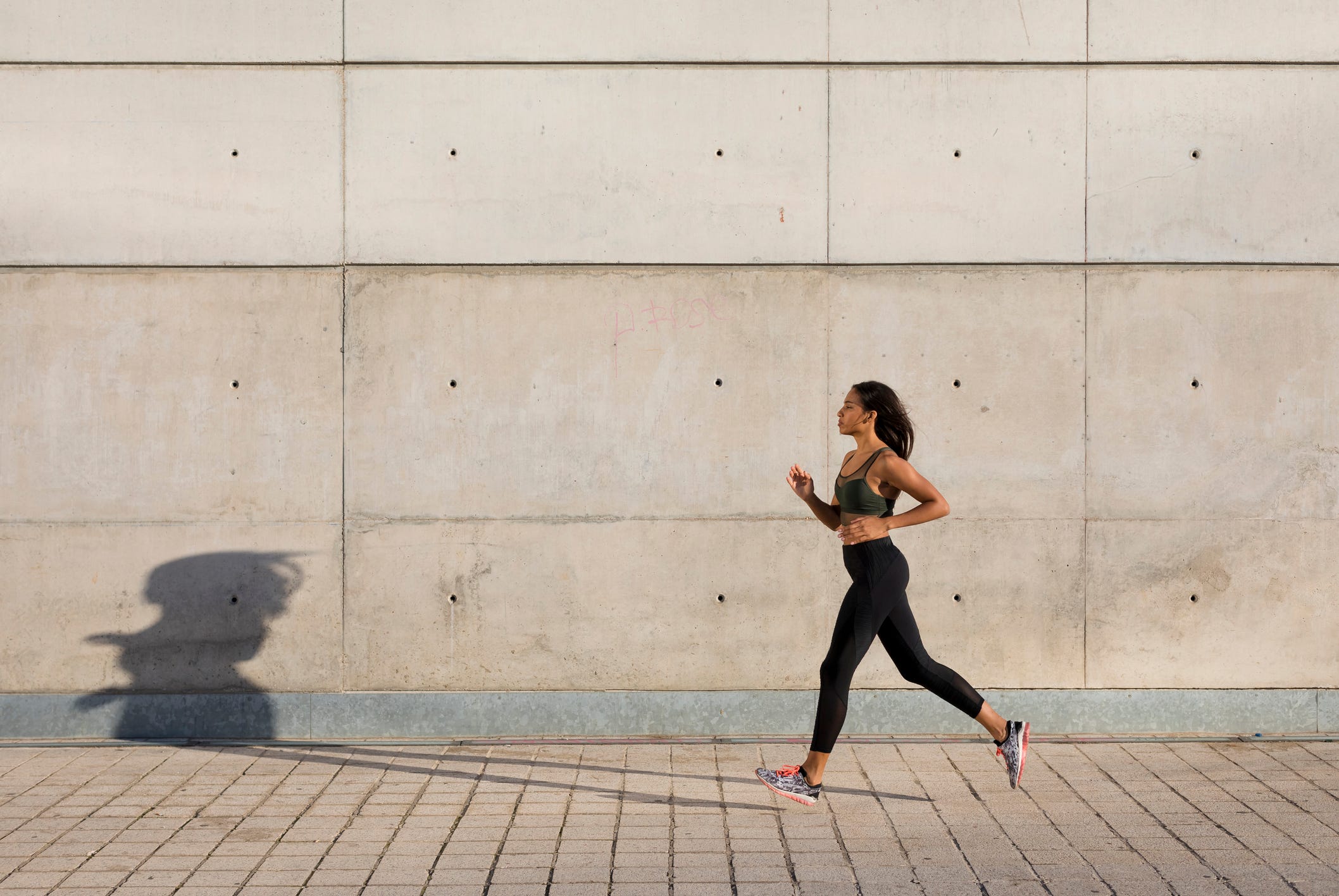 Young woman running along concrete wall in the city