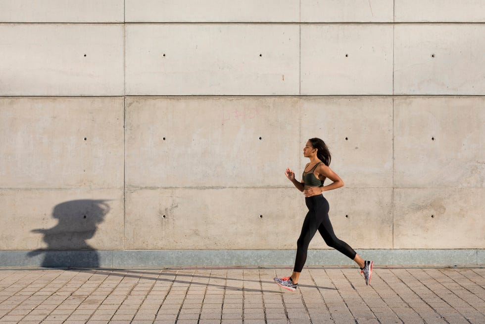 Young woman running along concrete wall in the city