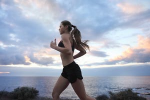 young woman running near ocean with cloudy sky