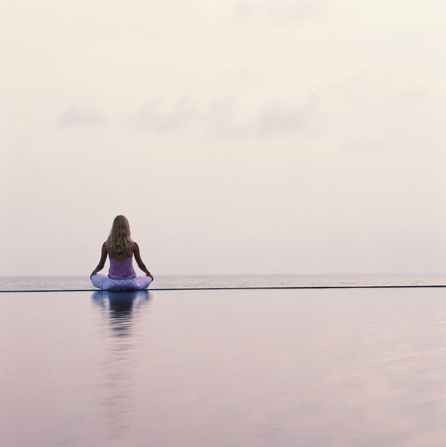 young woman sitting at side of pool, facing ocean, rear view