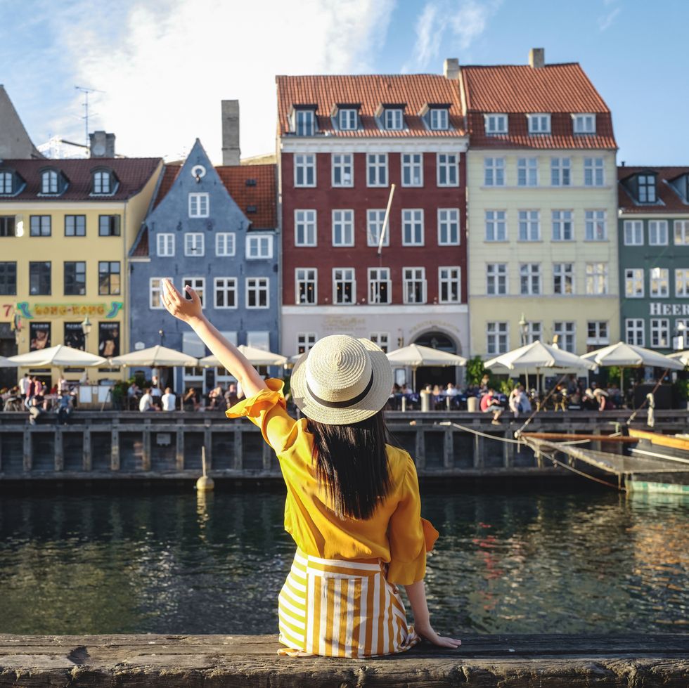 Young woman sitting in front of colorful buildings along Nyhavn (New Harbour), Copenhagen, Denmark