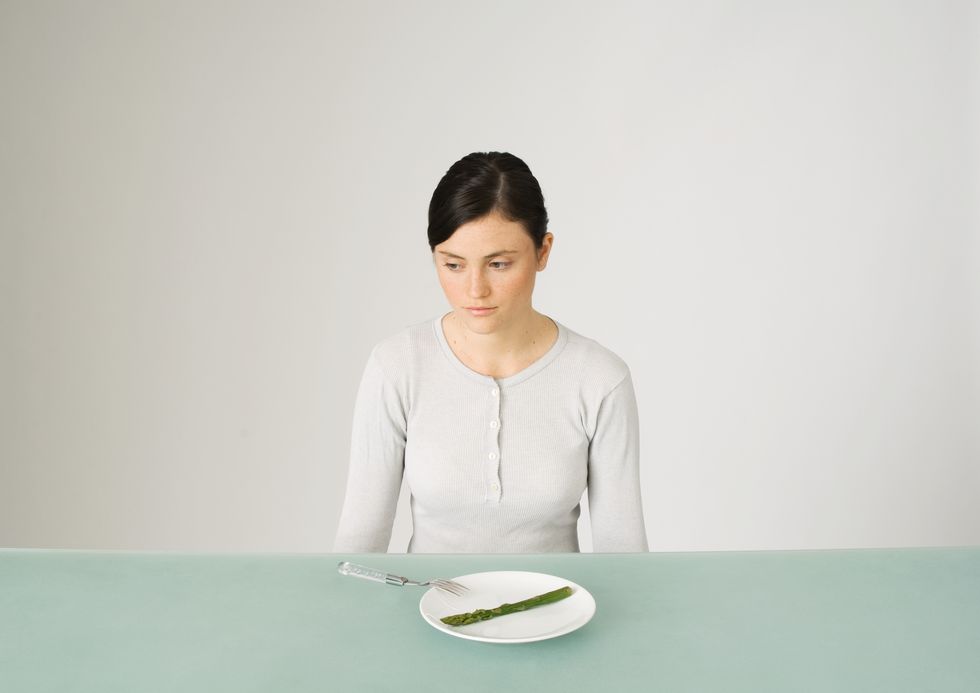 young woman sitting in front of plate with single asparagus, looking away