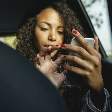 young woman sitting on back seat of a car using smartphone