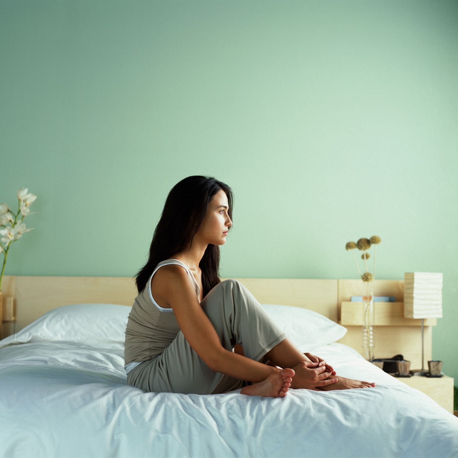 Young woman sitting on bed, side view